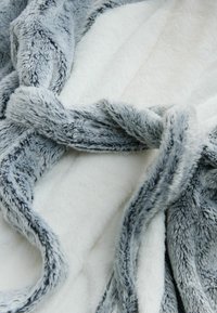 Zachte, pluche deken met grijze gestructureerde randen en gladde witte binnenstof, losgevouwen om de contrasterende materialen en kleuren te tonen.