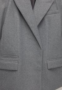 Blazer grigio in lana con rever a punta, due tasche frontali e una finitura morbida e testurizzata. Design sartoriale con silhouette strutturata.