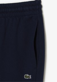 Marineblaue Jogginghose aus weichem Stoff, mit elastischem Bund und seitlichen Taschen. Besticktes grünes Krokodil-Logo auf dem Oberschenkel.