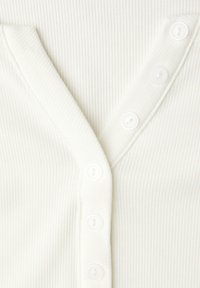 Wit geribd topje met een V-hals en vijf witte knopen aan de voorkant. De stof heeft een gestructureerd, rekbaar uiterlijk.