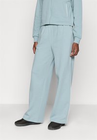 Lyseblå bomulls joggebukser med løs passform, elastisk midje og sidelommer. Skoene er svarte med en strukturert overflate.