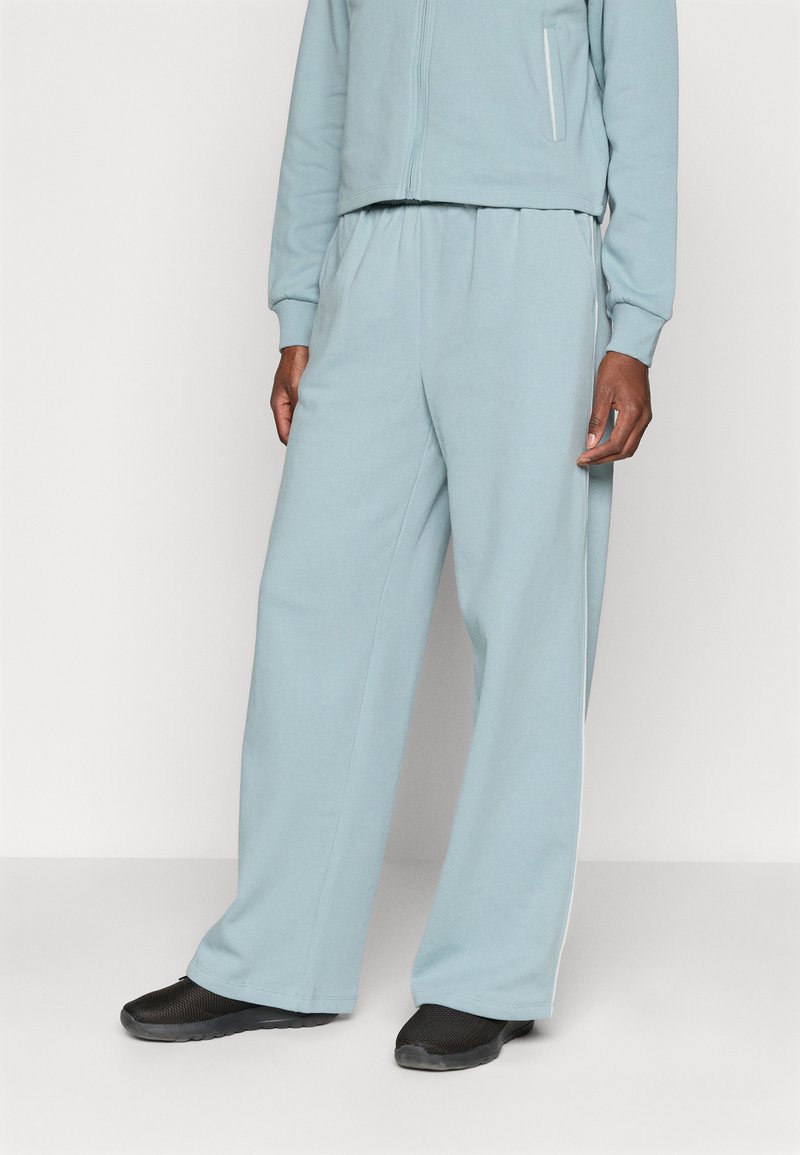 Lyseblå bomulls joggebukser med løs passform, elastisk midje og sidelommer. Skoene er svarte med en strukturert overflate.