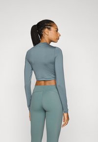 Långärmad, kort topp i dämpad tealfärg med en slät textur, tillsammans med matchande högmidjade leggings som betonar en strömlinjeformad passform.