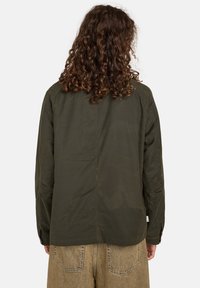 Dunkelolivgrünes Langarmhemd mit geradem Schnitt, mit Knopfmanschetten und einem schlichten Rückendesign. Der Stoff wirkt glatt mit minimaler Textur.