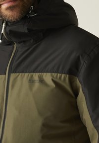 Hombre barbudo con una chaqueta Regatta Great Outdoors de dos tonos, verde y negro, con cremallera frontal y capucha.