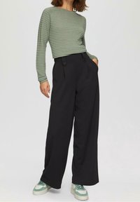 Grönrandig långärmad skjorta med rund hals, tillsammans med högmidjade svarta vida byxor med dubbelknappdetalj och fickor.