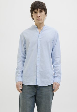 Camicia azzurra a maniche lunghe con colletto alla coreana, chiusura a bottoni e vestibilità comoda, realizzata in un tessuto texturizzato. Indossata con jeans blu.