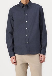 Camicia blu navy con colletto, maniche lunghe e tessuto testurizzato. Dotata di bottoni bianchi e di un taglio dritto all'orlo.