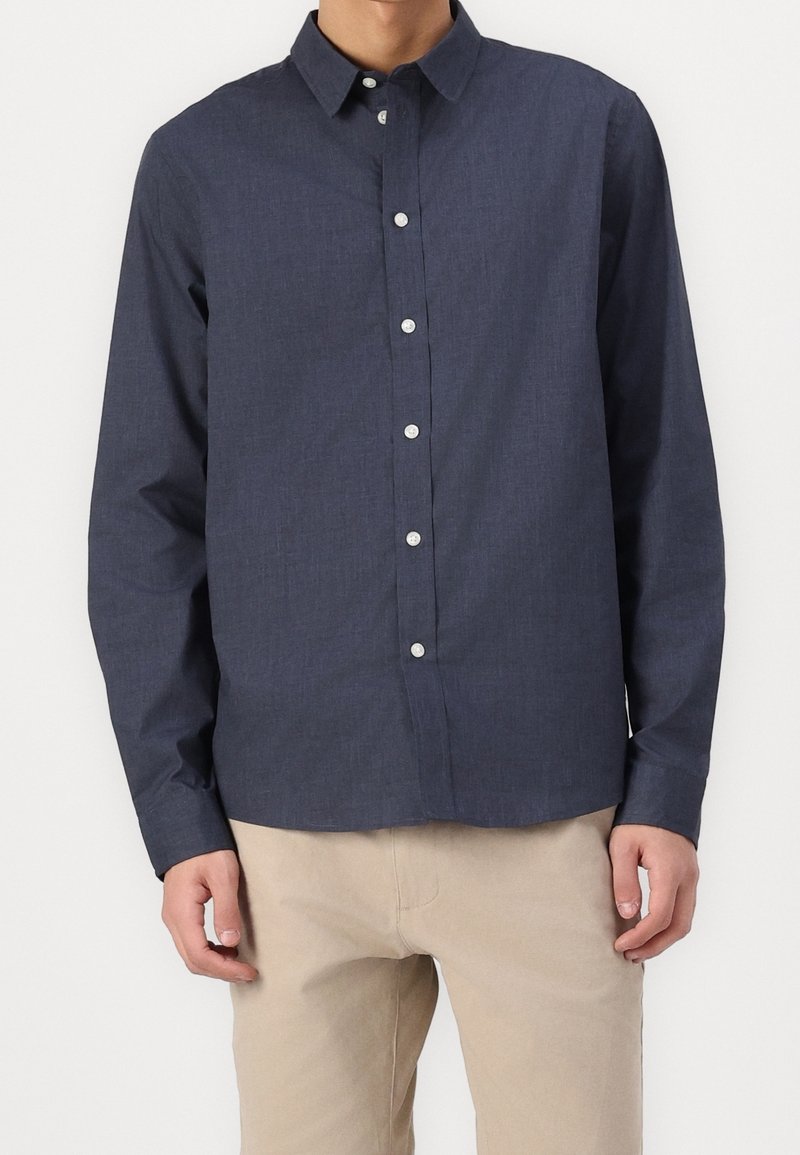 Camicia blu navy con colletto, maniche lunghe e tessuto testurizzato. Dotata di bottoni bianchi e di un taglio dritto all'orlo.