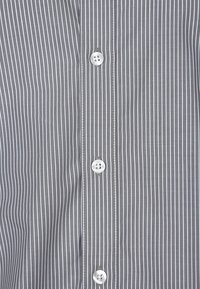 Camicia a righe grigie con strisce verticali bianche, dotata di quattro bottoni bianchi e un tessuto liscio e intrecciato.
