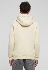 Beige hettegenser med en myk tekstur, med ribbestrikkede mansjetter og kant. Bakre visning viser et enkelt, rent design.