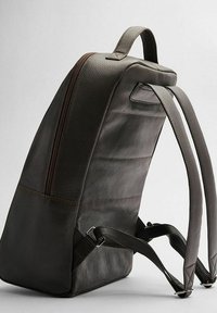 Mörkbrun läderryggsäck med en slät yta, utrustad med justerbara axelremmar, ett handtag på toppen och en dragkedjeförsedd framficka.