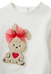 Indumento bianco con applicazione di coniglio beige testurizzato, cuore rosso e fiocco in tulle rosso sulla testa, cuciture dettagliate lungo i bordi.