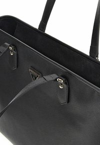 Sac fourre-tout noir texturé avec deux anses, accents en métal et plaque de logo. Présente une forme structurée et un design à ouverture supérieure.