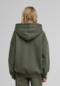 Oliivivihreä suuri huppari, jossa on suuri huppu, leveät hihat sekä ribbitetyt hihansuut ja helma. Valmistettu pehmeästä materiaalista, jossa on sileä pinta.