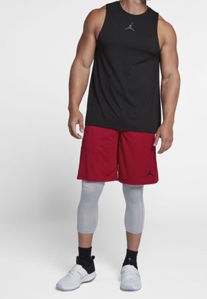 Débardeur noir sans manches avec logo gris, shorts rouges, leggings de compression gris clair et chaussures de sport noires à semelles blanches.