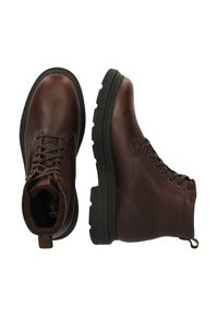 Bruna läderankleboots med en texturerad yta, rund tå, snörning och tjocka svarta gummisålar. Inkluderar en dragflik bak.