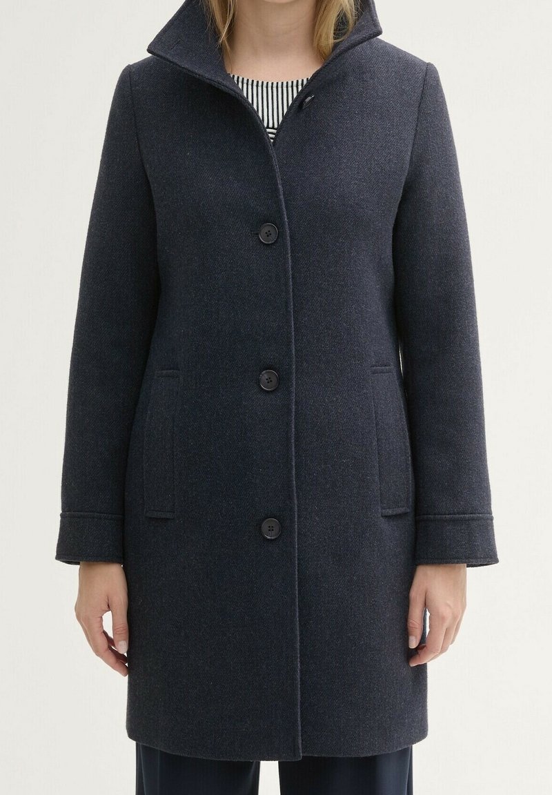 Abrigo de mezcla de lana de color azul marino oscuro con un cuello alto, seis botones, dos bolsillos laterales y mangas largas, con una tela texturizada.