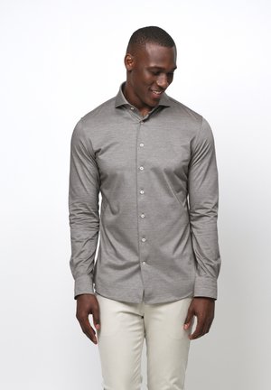 Hellgraues Langarmshirt mit Slim-Fit, das über einen Knopfleistenverschluss verfügt und aus einem glatten, strukturierten Stoff besteht. Kombiniert mit hellen Hosen.