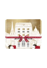 Un bâtiment de style parisien enveloppé d'un ruban rouge et d'un nœud, présentant des produits de soin de L'Oréal Paris et des feux d'artifice dans une palette de couleurs dorée et blanche.