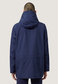 Marineblauwe waterdichte jas met een capuchon; heeft een rechte snit, elastische manchetten en een koord in de taille voor een verstelbare pasvorm.