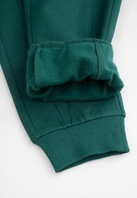 Zielone bawełniane dresy o miękkim, szczotkowym wnętrzu, z prążkowanymi mankietami i gładką teksturą tkaniny, prezentujące staranne detale szwów.