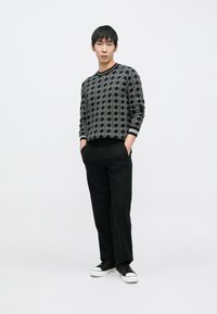 Juodas megztinis su balta geometrine rašto, apvaliu kaklu ir ribuotomis rankogaliais. Derinamas su juodomis kelnėmis ir juodais sportbačiais.