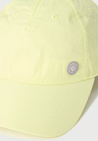 Ανοιχτόκίτρινο καπέλο μπέιζμπολ με ραμμένες τρύπες αερισμού και μικρό στρογγυλό γκρι λογότυπο της Columbia Sportswear στο πλάι.