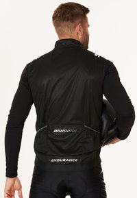 Svart cykelväst med en åtsittande design, zip-fodrat bakfack, reflexdetaljer och hög krage, ihop med en långärmad tröja.
