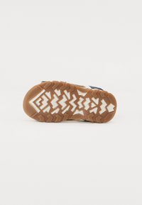 Rubber outsole with triangular tread pattern, featuring a brown base and white accents. Slightly textured surface for grip and traction.