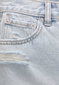 Denim bleu clair usé avec des bords effilochés, doté d'une fermeture à bouton et d'une couture dorée le long de la ceinture et des poches.