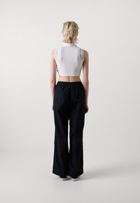 Débardeur blanc court avec un col haut ; associé à un pantalon noir à jambes larges avec des poches latérales et une taille élastique. Chaussures décontractées visibles.