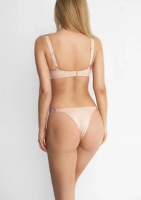 Jasnoróżowy zestaw bielizny z gładkiej, jedwabistej tkaniny. Biustonosz ma regulowane ramiączka oraz zapięcie na haftkę. Stringi mają detale z logo.