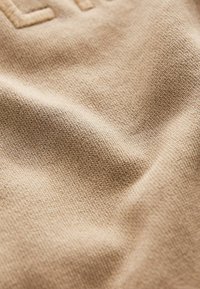 Stickad beige tyg med en mjuk textur, som visar en lätt lyster och subtil, upphöjd textdetalj.