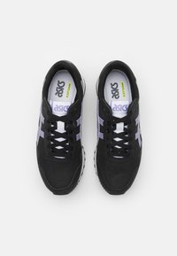 Svarte joggesko med grå og lilla detaljer, mesh-overdel, snøring, polstret tunge og hvit såle med teksturert mønster.