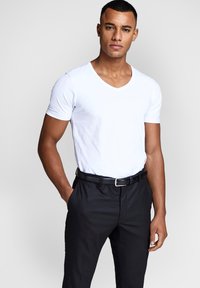 White cotton V-neck t-shirt paired with black trousers and a black belt. The outfit features a fitted design and smooth texture.