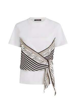 Λευκό κοντομάνικο τοπ με προσαρμοσμένο μαύρο και μπεζ ριγέ κασκόλ δεμένο στη μέση, με αφηρημένο σχέδιο γραφής.