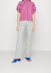 Blusa rosa a maniche a sbuffo con colletto e decorazioni nere abbinata a jeans flare azzurri e sandali con tacco blu.