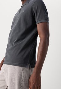 Tmavě šedá polokošile s jemnou texturou, která má dvoubarevné zapínání a krátké rukávy. Na hrudi je decentní logo.