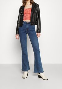 Giacca moto in pelle nera, top cropped floreale rosso, jeans a vita alta blu svasati, stivaletti bianchi con tacco, outfit urbano casual.