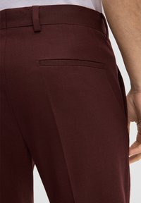 Bordeauxkleurige broek van gladde stof met een getailleerde pasvorm, voorzien van een achterzak en een tailleband voor een veilige pasvorm.