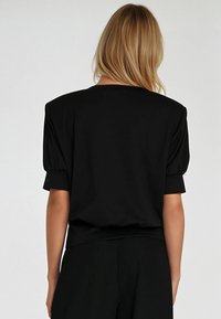 Czarna bluzka z krótkimi, bufkami i luźnym krojem. Materiał wydaje się miękki, o gładkiej fakturze i starannie wykończonych szwach.