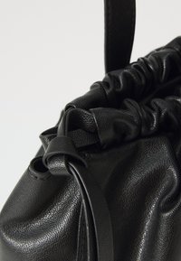 Schwarze Leder-Zugtasche mit strukturiertem Oberflächen, gerafftem oberen Teil und schlankem Tragegurt. Keine sichtbaren Beschläge oder Akzente.