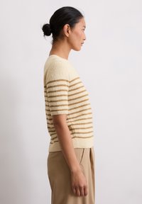 Kremowy sweter w poziome brązowe paski, z krótkimi rękawami i miękką fakturą. Prosty, okrągły dekolt i dopasowany dół.