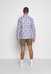 Ljusblå skjorta med vit ikatmönster, långa ärmar och krage. Bärs med bruna shorts och vita skor.