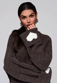 Brązowy sweter z dzianiny z długimi rękawami, z białym wzorem serca na mankietach. Miękka faktura i luźny krój.