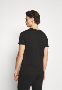 Tricou negru din bumbac cu mâneci scurte, gât rotund și un design ajustat, văzut din spate. Textură netedă, stil minimalist.