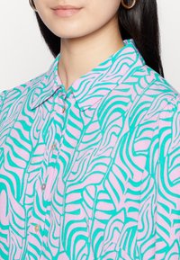 Camisa leve com um padrão abstrato ondulado em rosa e turquesa. Colarinho clássico com fecho de botão, textura de tecido suave.