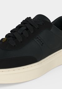 Μαύρο sneaker χαμηλού τύπου με μαύρες κορδόνια, ανάγλυφο λογότυπο BOSS στην πλευρά και παχύ λευκό πέλμα με ορατές ραφές.