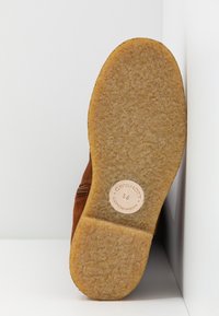 Semelle d'une chaussure en daim marron avec une semelle extérieure en caoutchouc beige texturée et une étiquette circulaire indiquant "CQS HOTT 36 Copenhague".
